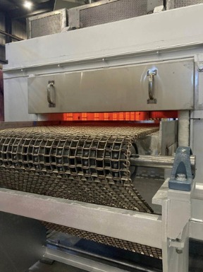 Tunnel oven discharge with mesh oven conveyor belt and heating elements in an industrial bakery