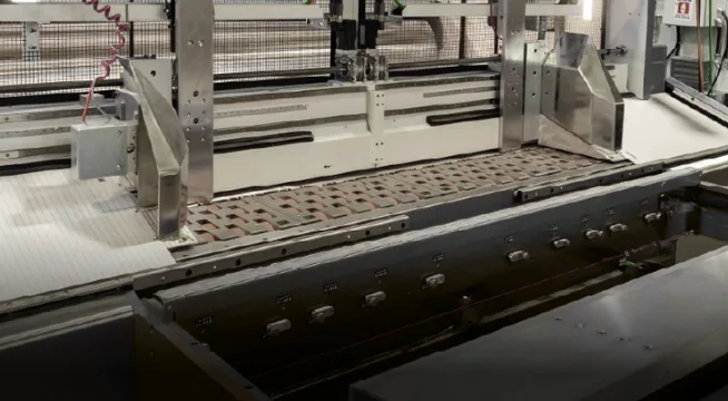 Converting line vacuum transfer conveyor feeding corrugated board through a folder-gluer section
